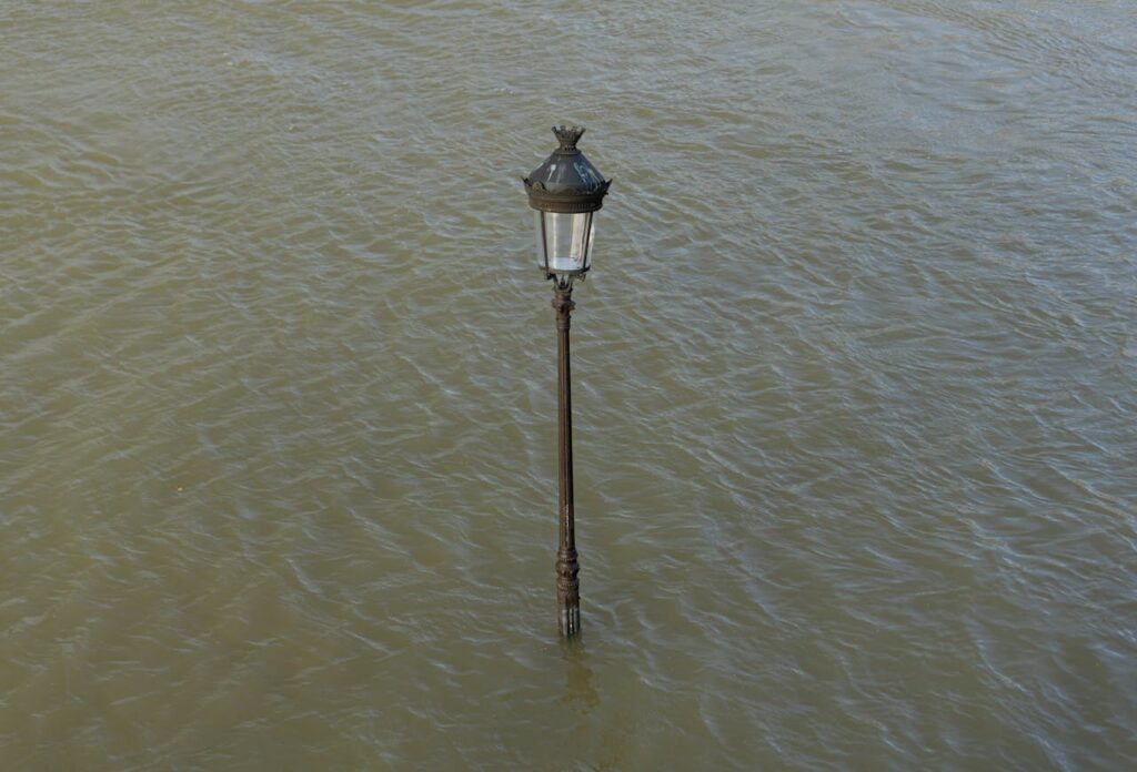 A lone streetlamp is submerged in flood waters, highlighting the impact of urban flooding.