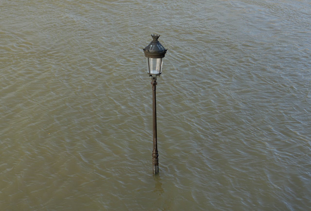 A lone streetlamp is submerged in flood waters, highlighting the impact of urban flooding.