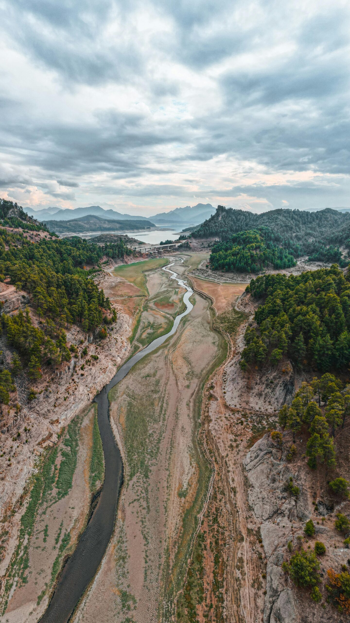 Aerial shot of a dry riverbed in a canyon during the day, surrounded by lush greenery and mountains.